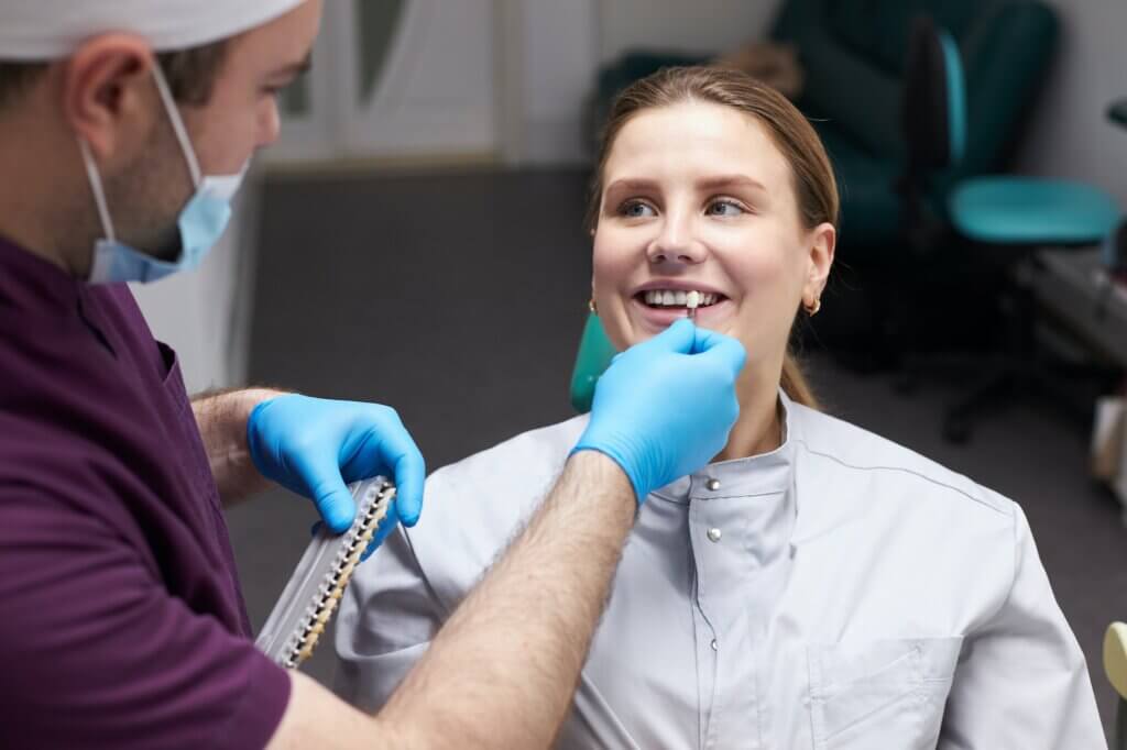 Dentist aplică nuanță pe dinții pacientului zâmbind.